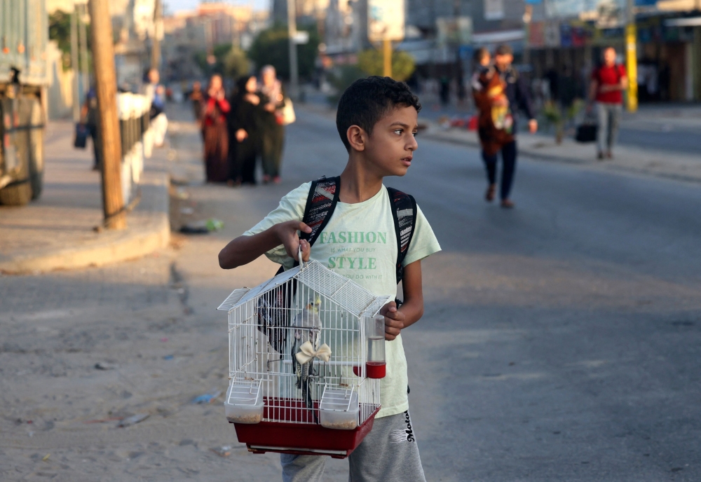 A Palestinian boy carries his pet bird in a cage as families leave their homes following an Israeli attack on the Rafah refugee camp, in the southern of Gaza Strip. — AFP pic