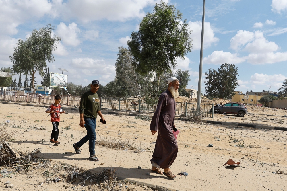 Palestinians walk near a damaged car, after Israeli strikes, in Rafah in the southern Gaza Strip October 17, 2023. — Reuters pic
