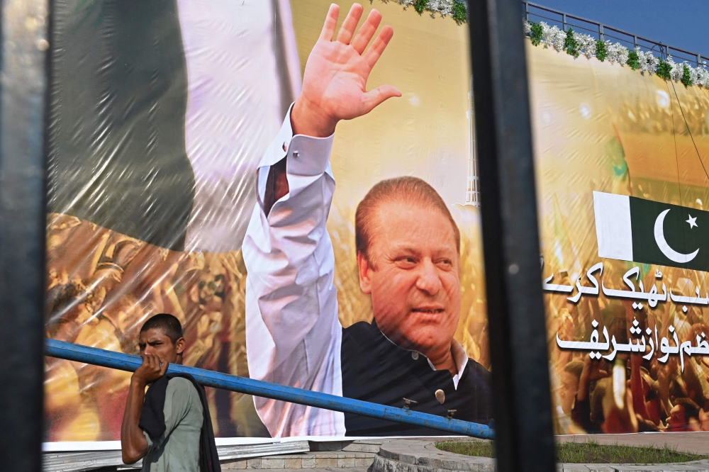 A labourer walks past a large banner of Pakistan's former Prime Minister Nawaz Sharif displayed at a park ahead of his arrival in Lahore on October 19, 2023. — AFP pic