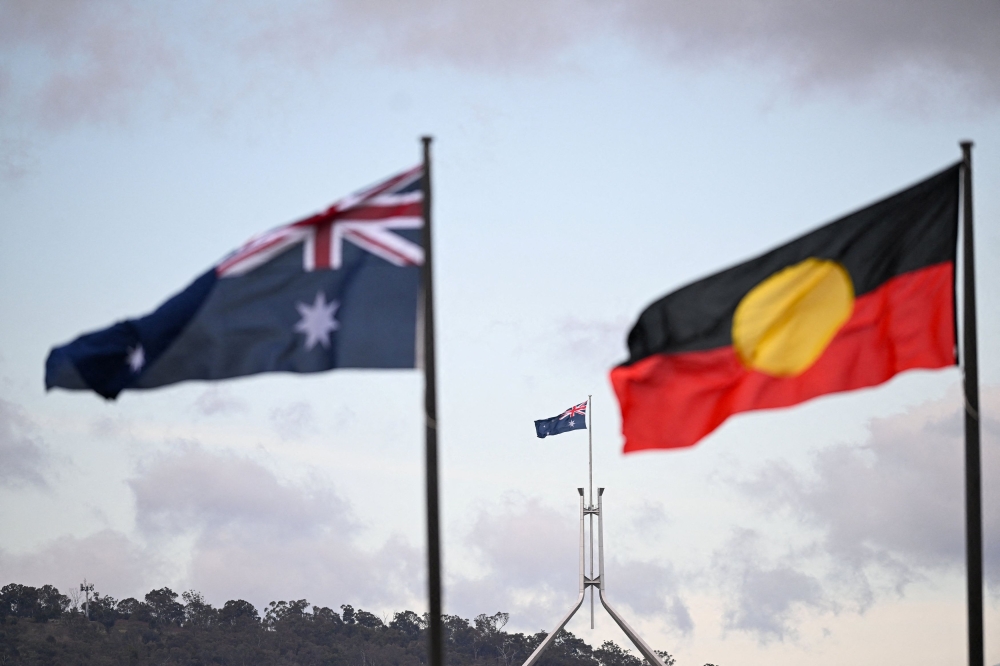 The Australian Parliament House is seen behind the Australian flag and the Indigenous flag in Canberra October 14, 2023. A 16-year-old Aboriginal boy has died a week after he was found ‘unresponsive’ in youth detention, authorities said today. — AAP Image/Lukas Coch via Reuters pic