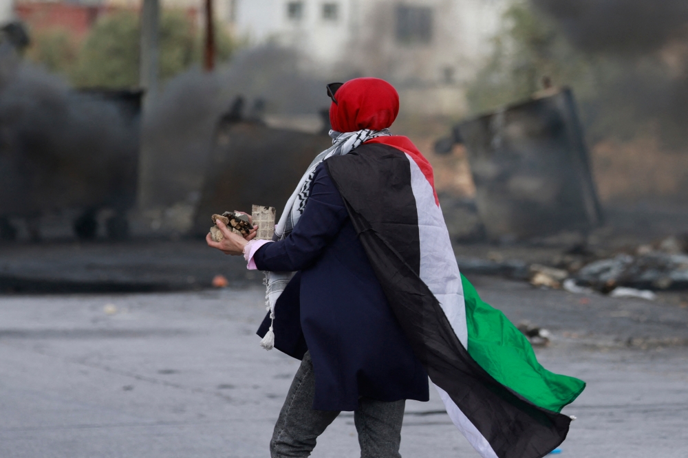 A woman draped in a Palestinian flag prepares to hurl stones toward Israeli forces during clashes with them at the northern entrance of the West Bank city of Ramallah near the Israeli settlement of Beit El on October 20, 2023, as battles continue between Israel and the Palestinian Hamas group. — AFP pic