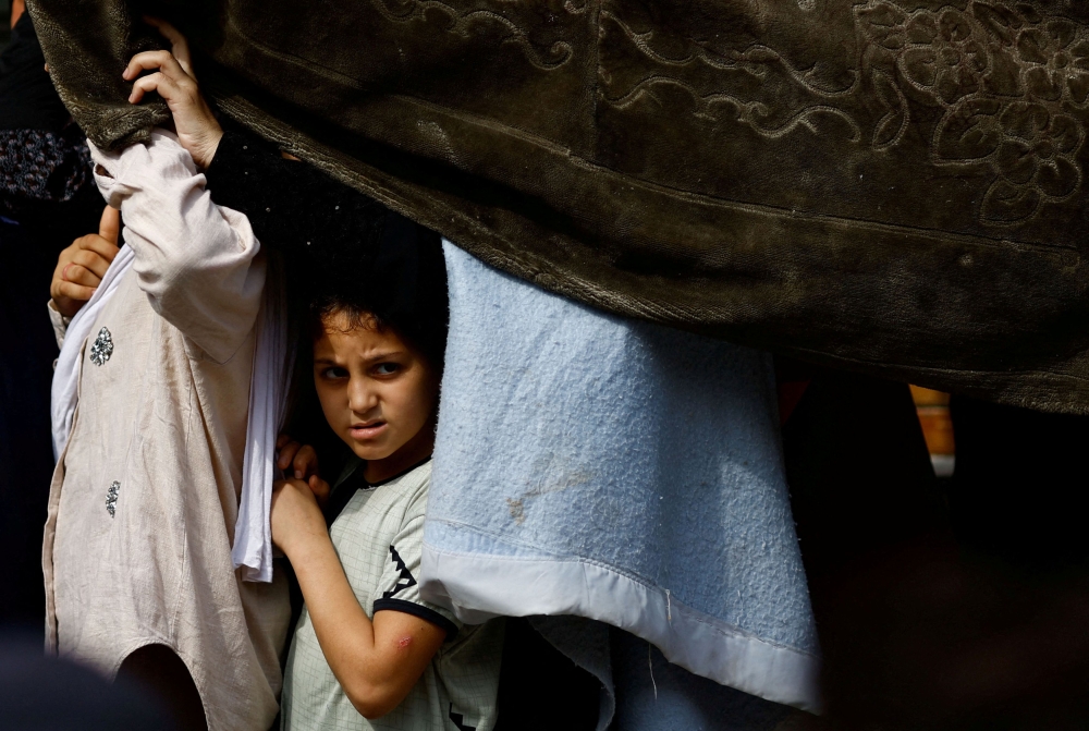 A child looks on as Palestinians queue to buy bread from a bakery, amid shortages of food supplies and fuel, as the conflict between Israel and Palestinian Islamist group Hamas continues, in Khan Younis in the southern Gaza Strip October 22, 2023. — Reuters pic