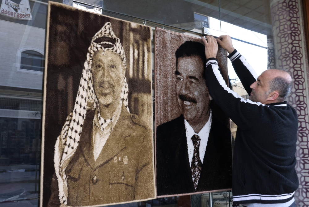 A shop owner in the West Bank city of Hebron on November 10, 2022, hangs a portrait of the late Iraqi president Saddam Hussein (right) next to one of late Palestinian leader Yasser Arafat. — AFP pic