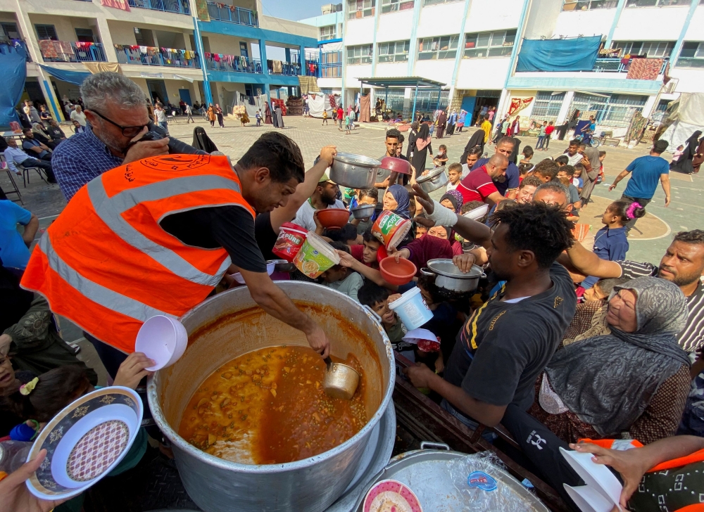 Palestinians, who fled their houses due to Israeli strikes, gather to get their share of charity food offered by volunteers, amid food shortages, at a UN-run school where they take refuge, in Rafah, in the southern Gaza Strip, October 23, 2023. — Reuters pic 