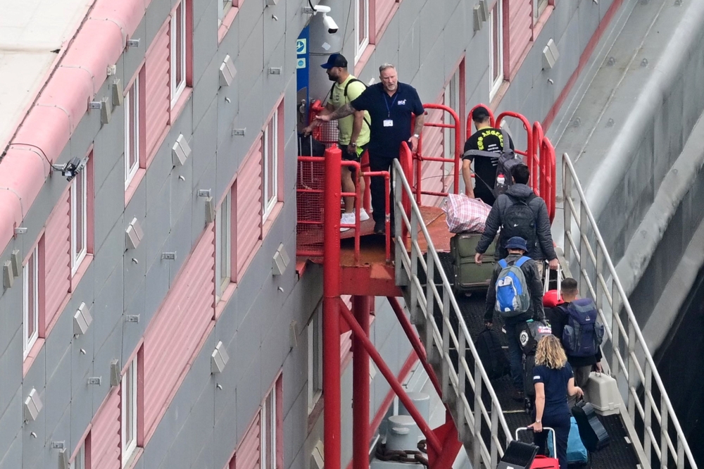 People carrying bags are seen walking up the gangway into the Bibby Stockholm accommodation barge, moored to the quayside at Portland Port in Portland, on the south-west coast of England. — AFP pic