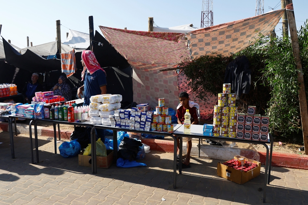 A Palestinian boy sits by produce, as Palestinians who fled their houses amid Israeli strikes, take shelter at a tent camp at a United Nations-run centre, after Israel's call for more than 1 million civilians in northern Gaza to move south, in Khan Younis in the southern Gaza Strip, October 26, 2023. — Reuters pic