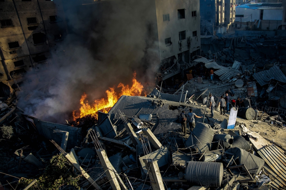 Palestinians stand on the rubble of a levelled building as smoke and fire rise from the destruction following an Israeli strike in Gaza City on October 26, 2023, amid battles between Israel and the Palestinian group Hamas. — AFP pic