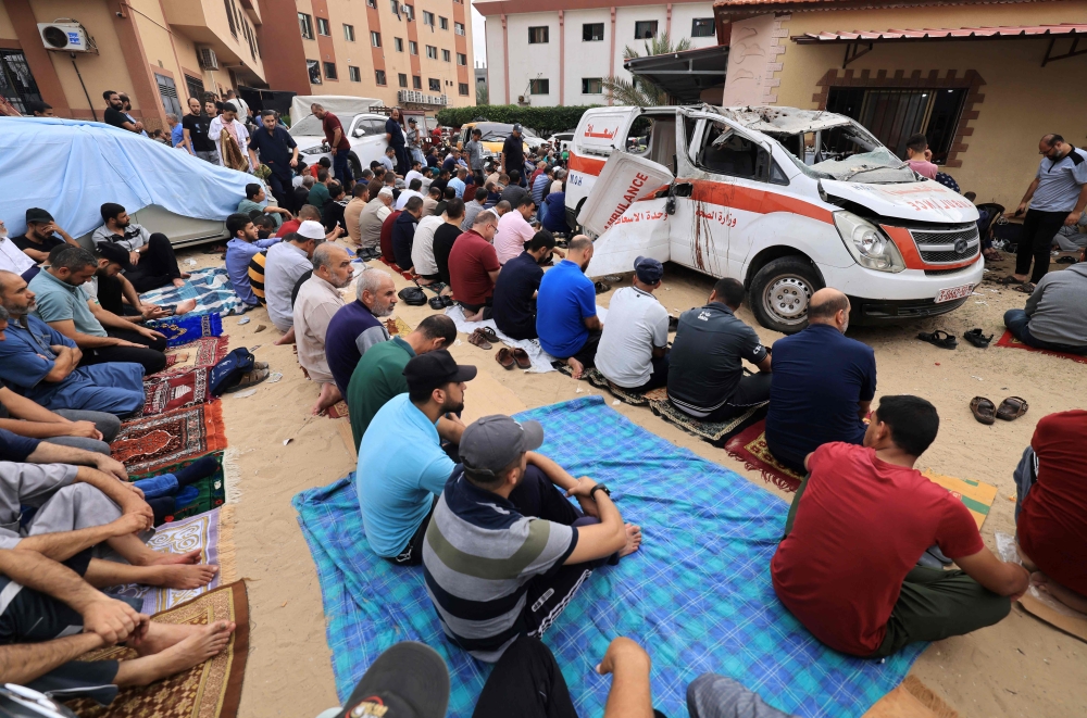 Palestinian men, seated on the ground close to a damaged ambulance, take part in Friday Noon prayers in the drive way of the emergency entrance of the Nasser hospital in Khan Yunis, in the southern Gaza Strip on October 27 , 2023, amid the ongoing battles between Israel and the Palestinian group Hamas. — AFP pic