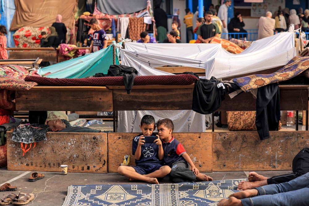 Children playing a game on a mobile phone in the playground of a school run by the United Nations Relief and Works Agency for Palestine Refugees (UNRWA) agency that has been converted into a shelter for displaced Palestinians.