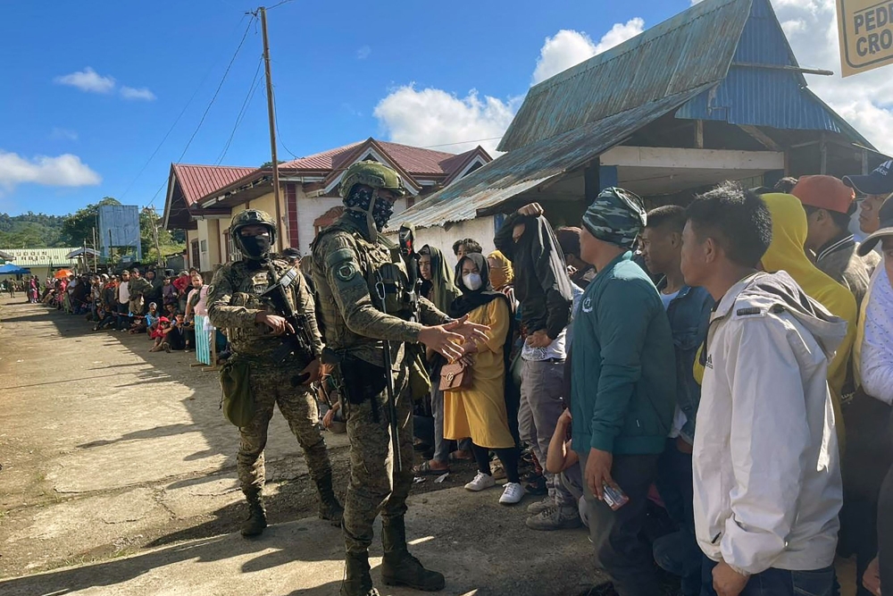 Soldiers stand guard as voters wait in line outside a polling station in Marawi, Mindanao island. — AFP pic