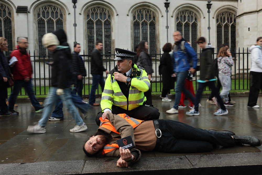 A Just Stop Oil climate activist is detained by a police officer after taking part in a slow march to disrupt traffic in London. — AFP pic