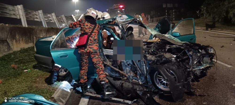 Firemen extricate the victims who were trapped inside the wrecked Proton Wira car after it crashed into a road barrier along Jalan Bukit Impian-Senai near Johor Baru, October 31, 2023. — Picture courtesy of the Johor Fire and Rescue Department