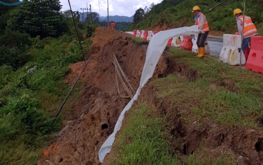 Workers place tarpaulin sheet over a landslide-struck section of the Bau-Lundu road on January 16, 2021. — Borneo Post pic 