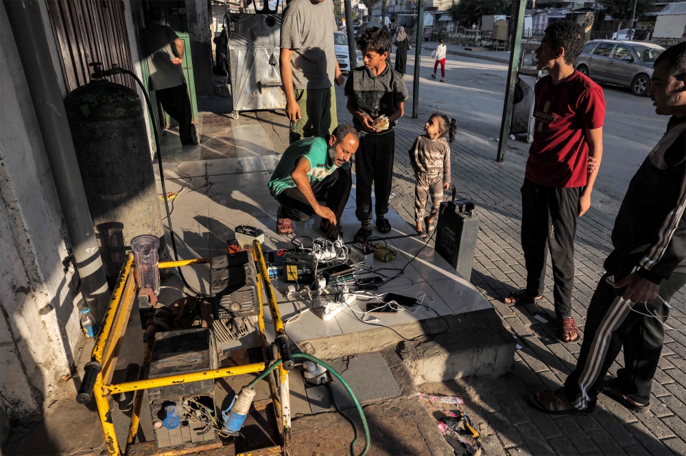 People gather around a charging station for cell phones, portable power supplies, and car batteries connected to a fuel-based electric generator on the side of a street in Rafah in the southern Gaza Strip on October 31, 2023 amid ongoing battles between Israel and the Palestinian Hamas movement. — AFP pic