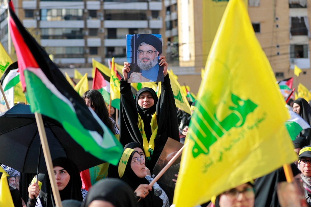 Supporters of the Lebanese Shiite movement Hezbollah wave flags as they watch a televised speech by its leader Hassan Nasrallah (unseen) in the Lebanese capital Beirut's southern suburbs on November 3, 2023. — AFP pic