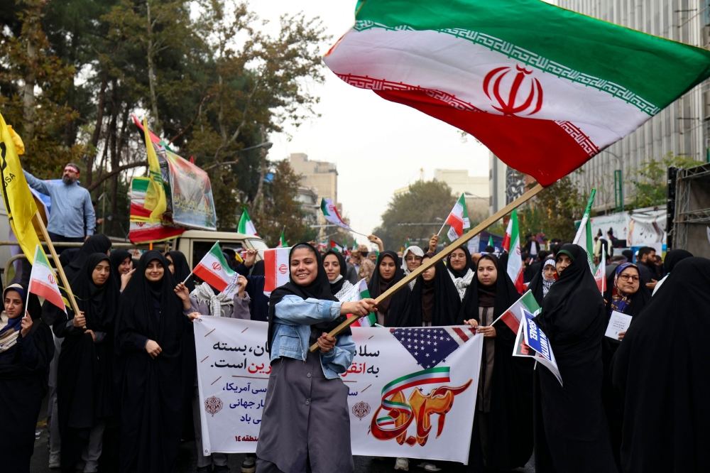 Iranian women wave their national flag during a rally outside the former US embassy in Tehran, to support the Palestinians of the Gaza Strip and to mark the 44th anniversary of the start of the Iran hostage crisis, on November 4, 2023. — AFP pic