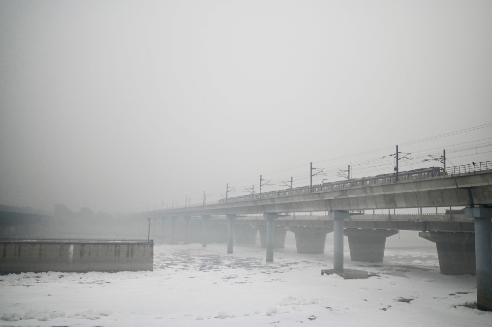 A metro train rides over a river choking with foul froth, amid heavy smog conditions in New Delhi on November 4, 2023. — AFP pic