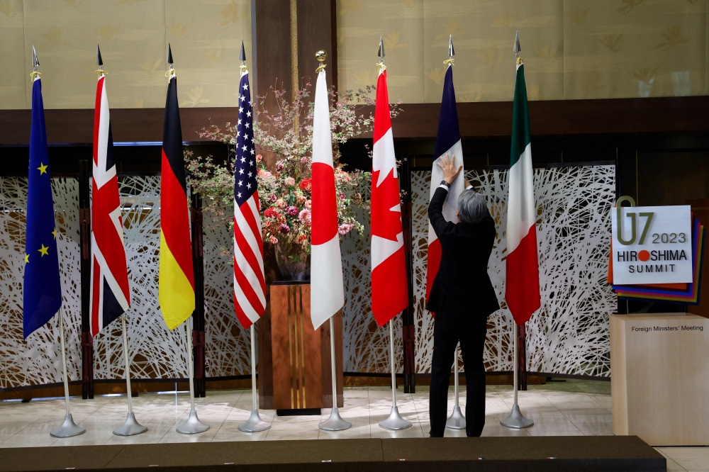 An official adjusts flags before G7 foreign ministers gather for a family photo during their meetings in Tokyo on November 8, 2023. — AFP pic