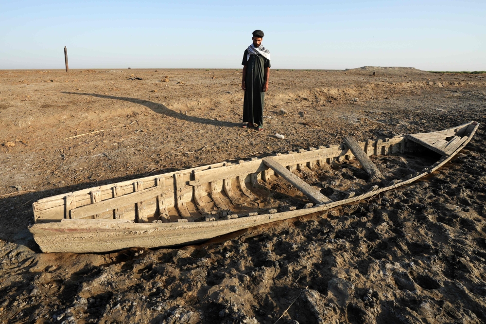 An Iraqi man looks at a grounded boat along a dried-up bank in the Chibayish marshes in Iraq's southern Dhi Qar province on June 25, 2023. — AFP pic