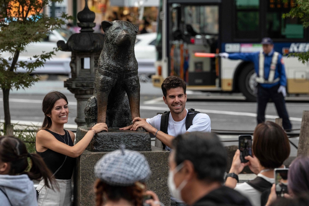 A couple pose for photos next to the statue of ‘Hachiko’ in front of Shibuya station in central Tokyo on November 6, 2023, ahead of the 100th anniversary of the legendary dog’s birth this month. — AFP pic 