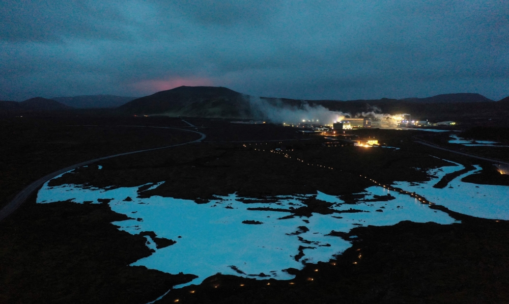 The red shimmer from magma is seen coming out from the erupting Fagradalsfjall volcano behind the tourist land mark Blue Lagoon, near the town of Grindavik  some 40 km west of the Icelandic capital Reykjavik, on March 20, 2021. — AFP pic