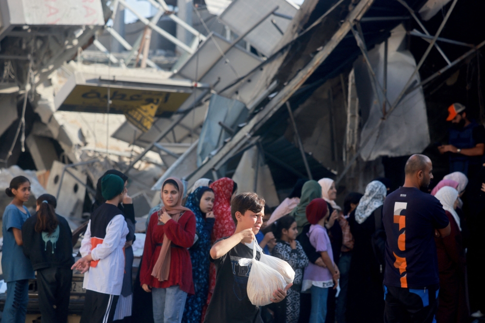 Palestinians queue up to buy fresh bread next to destroyed buildings at the Nuseirat refugee camp in central Gaza. — AFP pic