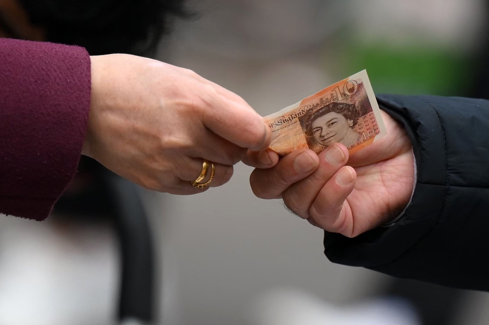A customer uses a ten pound note to pay for goods at a market in east London February 20, 2023. — AFP pic