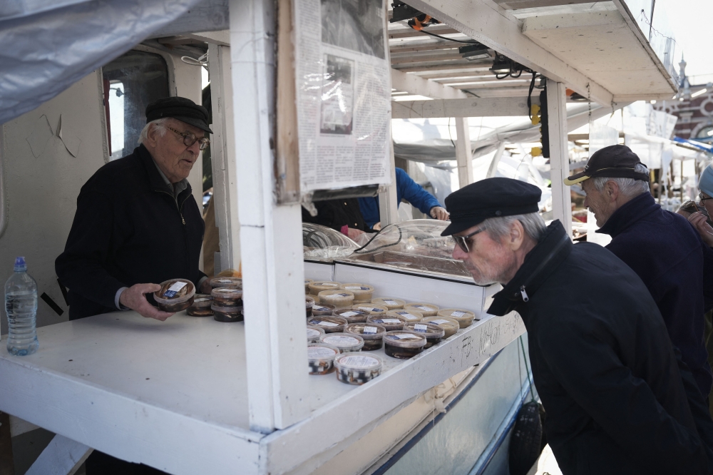Herring fisherman Holger Sjogren (left) sells herring products on his boat at the fish market in Helsinki, Finland on October 6, 2023. — AFP pic