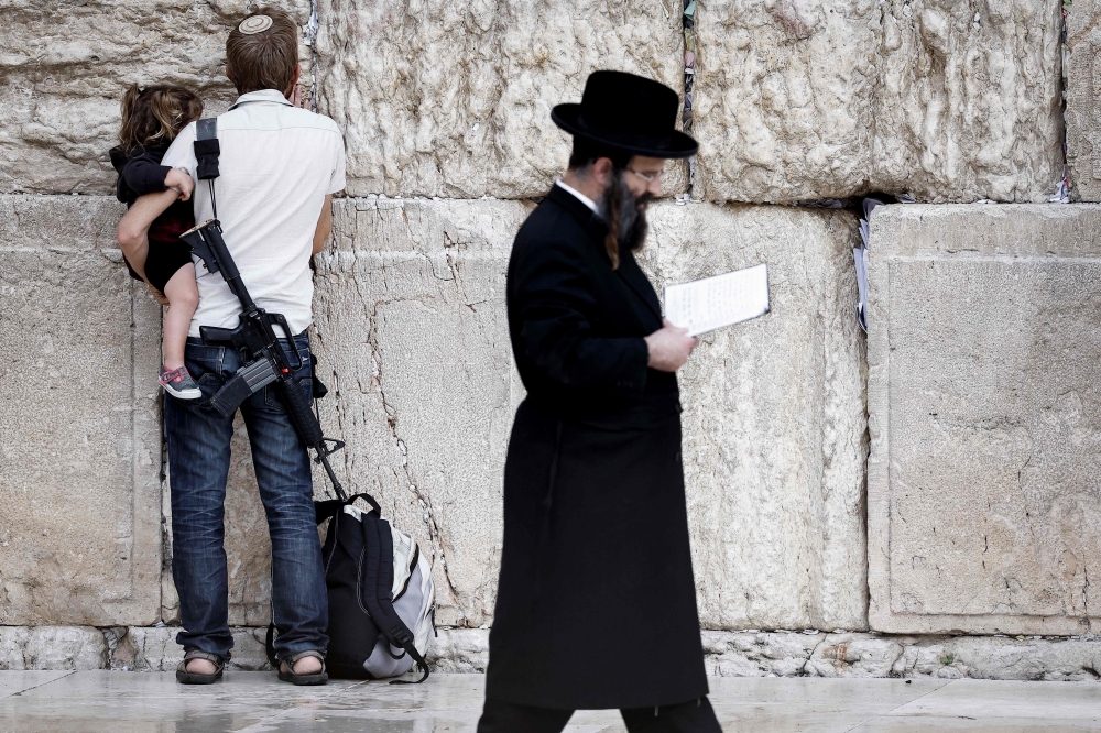 An armed Jewish man holds a child as he prays at the Western Wall, the last remaining vestige of the Second Temple, in Jerusalem’s Old City on November 12, 2023. — AFP pic