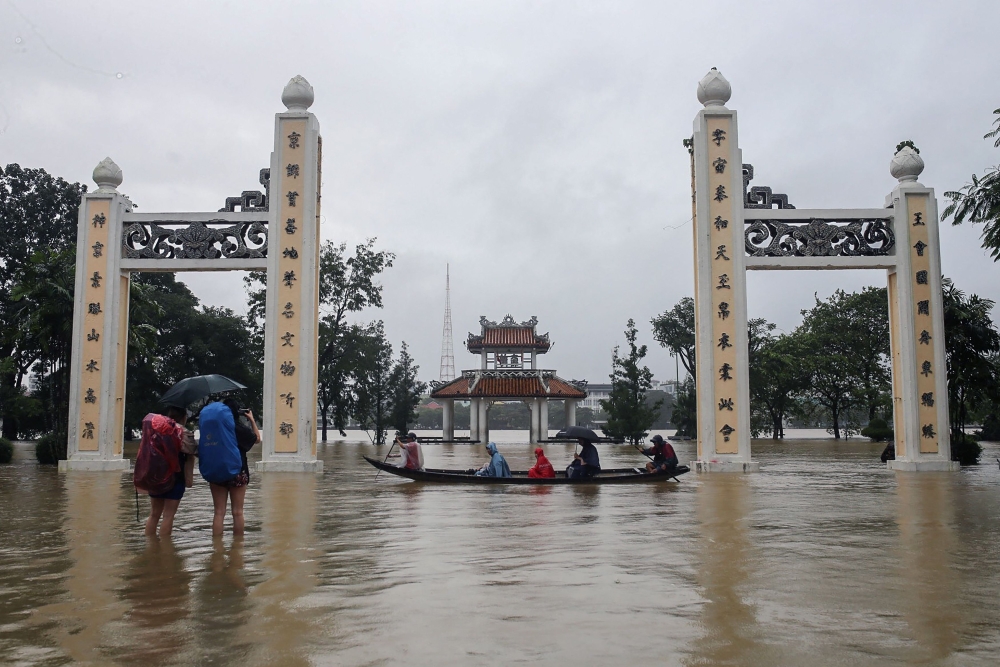 People ride on a boat and walk through a flooded area of Hue city in central Vietnam on November 15, 2023. — AFP pic