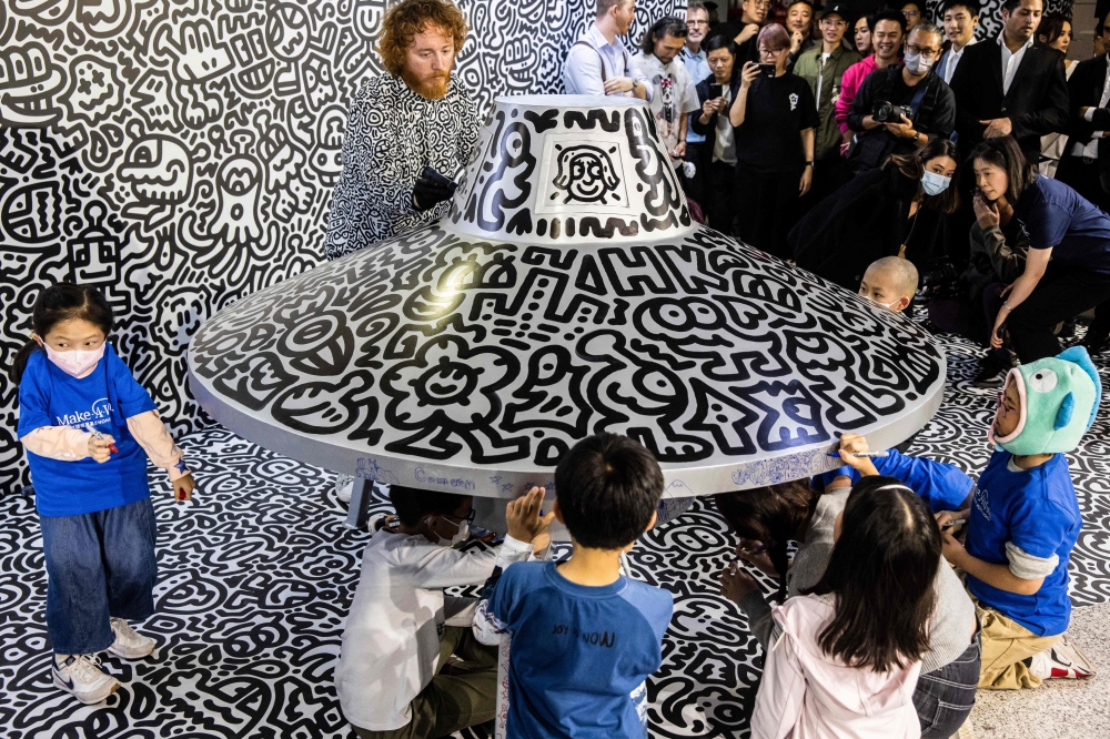 British artist Sam Cox (top), better known as Mr Doodle, draws on a model spaceship for a live art performance with children from Make-A-Wish Foundation at Central MTR Station in Hong Kong on November 19, 2023. — AFP pic