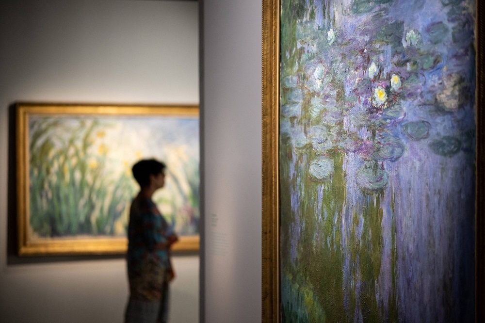 A woman passes by ‘Nympheas’ (right) a paint by French artist Claude Monet presented in the exhibition ‘Metamorphoses dans l’art de Claude Monet’, on June 15, 2022, at the Fontevraud modern art museum. — AFP pic