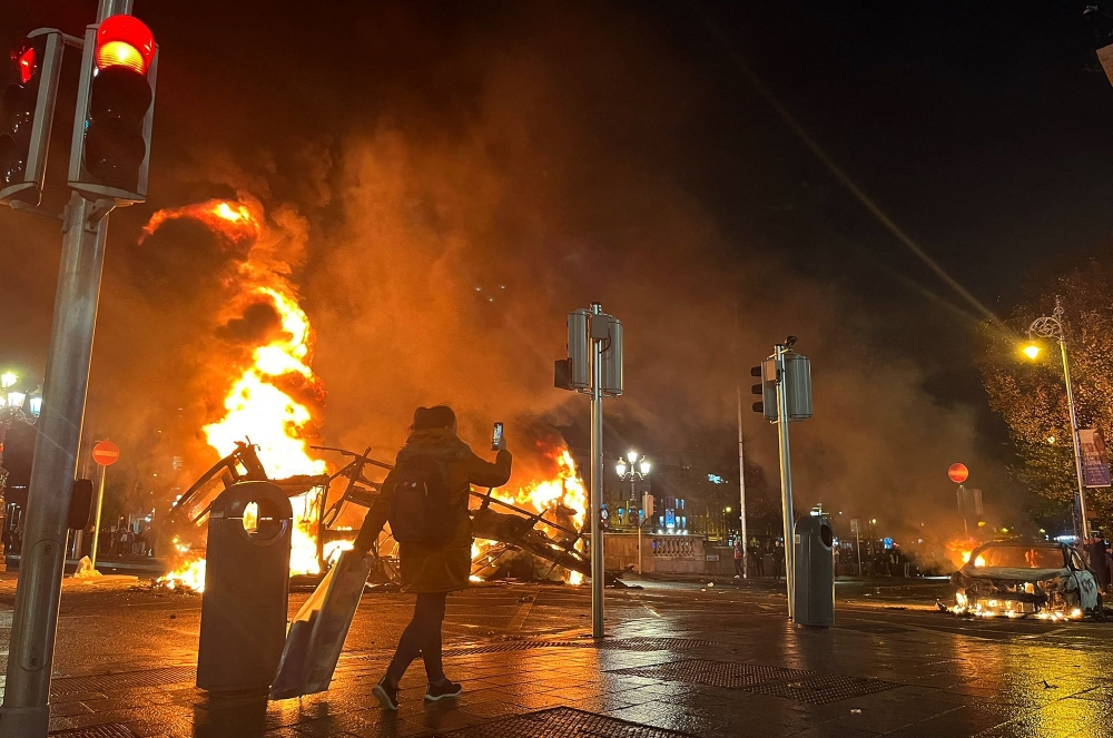 Flames rise from the car and a bus, set alight at the junction of Bachelors Walk and the O'Connell Bridge, in Dublin on November 23, 2023, as people took to the streets following the stabbings earlier in the day. — AFP pic
