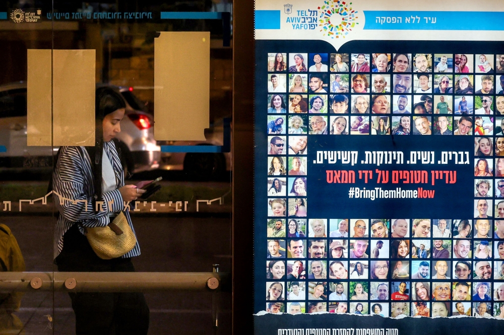 A woman stands at a bus stop in Tel Aviv near a combination of photos and a sign calling for the release of hostages held in the Gaza Strip by Hamas. — AFP pic
