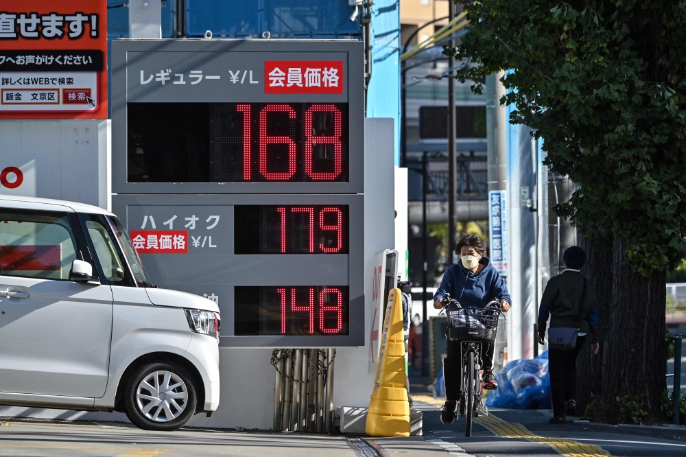 A woman cycles past a petrol station showing the price of a litre of regular at ¥168 along a street in Tokyo on November 24, 2023. ― AFP pic