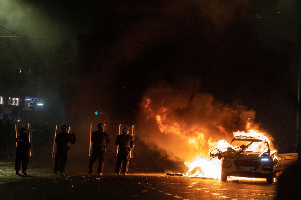 Riot police officers face down demonstrators next to a burning police car near a crime scene of a school stabbing that left several children and adults injured, in Dublin November 23, 2023. — Reuters pic