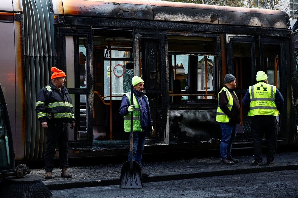 Workers stand in front of a burned-out tram, following a riot in the aftermath of a school stabbing that left several children and adults injured, in Dublin November 24, 2023. — Reuters pic