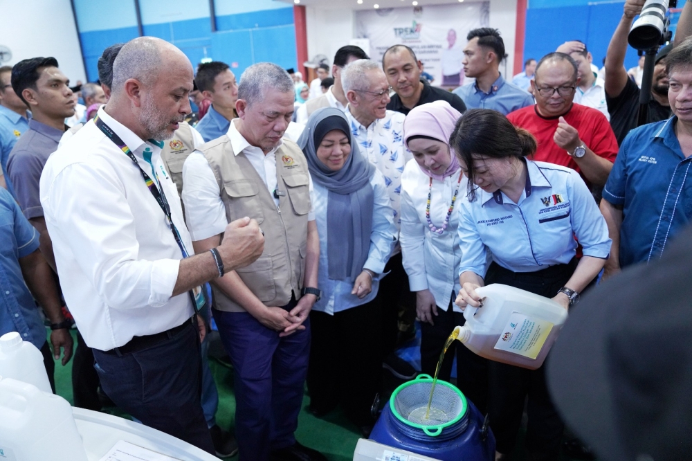 Fadillah (second left) being shown a demonstration of how the used cooking oil is collected. Accompanying him are Sharifah Hasidah (second right), Fazzrudin (back row, third right) and Ibrahim (back row, fourth right). — Borneo Post pic