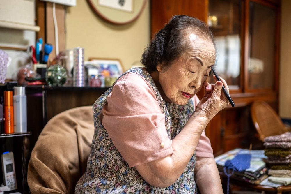 This picture taken on August 30, 2023 shows 100-year-old beauty advisor Tomoko Horino putting on makeup at her house before heading to the office in Fukushima city. — AFP pic