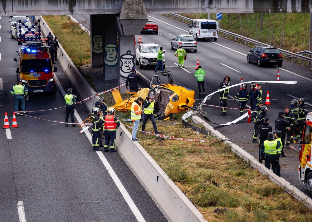 Emergency workers stand next to a helicopter that crashed on a Madrid motorway ring road, hitting a car and injuring people, in Madrid December 1, 2023. — Reuters pic