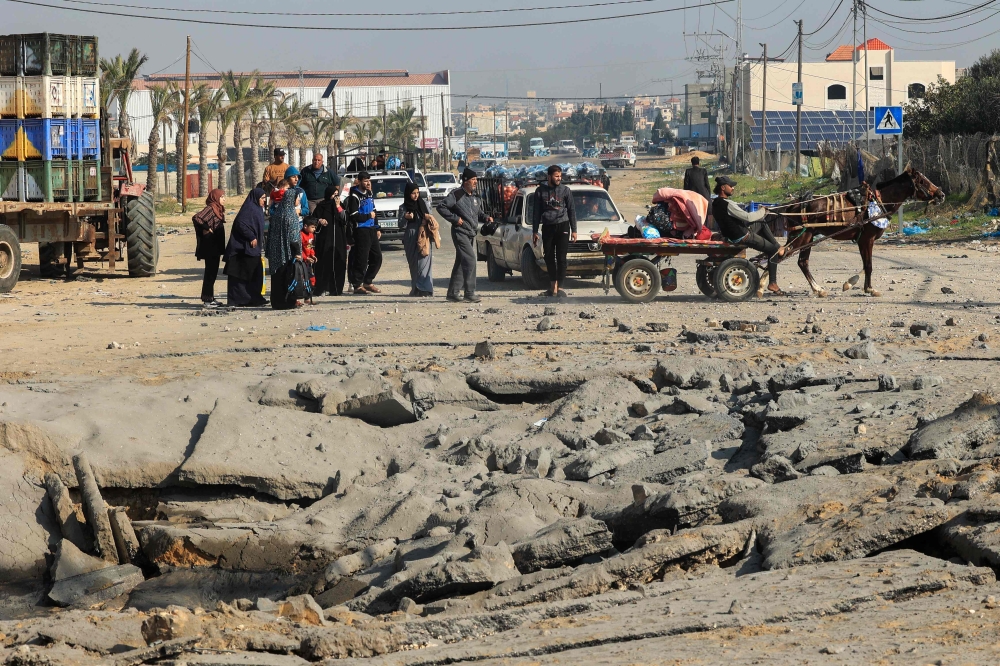 Palestinians stand next to a crater following an Israeli airstrike on the main road between Rafah and Khan Yunis on the southern Gaza Strip, on December 2, 2023, amid continuing battles between Israel and Hamas. — AFP pic