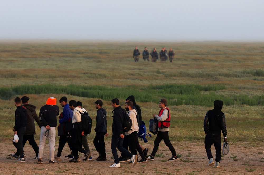 Migrants walk past gendarmes as they go back to their makeshift camp at sunrise after a failed attempt to cross the Channel to the UK on a small boat, in Grand-Fort-Philippe, near Calais, France, August 16, 2023. — Reuters pic