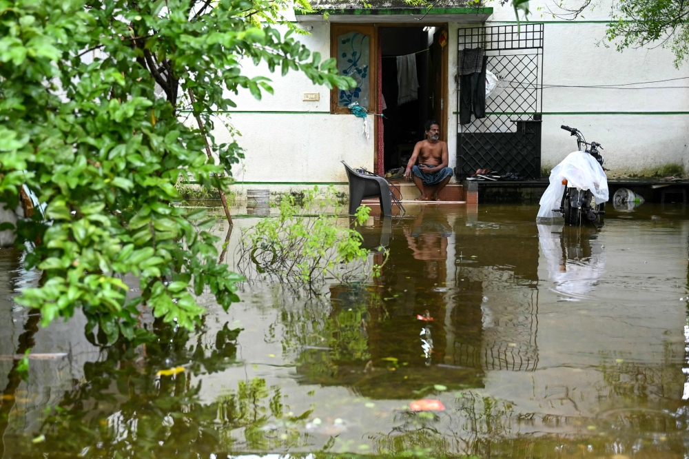 A man sits at his house in a flooded street after heavy rains ahead of Cyclone Michaung's landfall in Chennai on December 3, 2023. — AFP pic