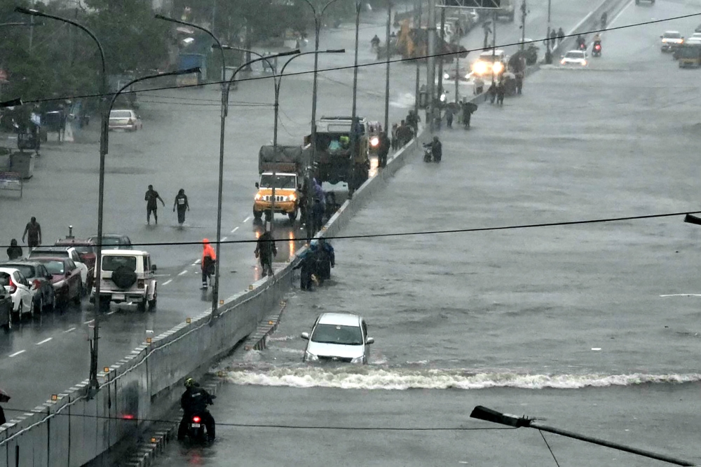 Commuters make their way through a flooded road after heavy rains in Chennai on December 4, 2023. — AFP pic