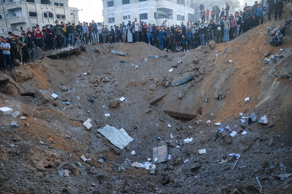 Palestinians stand on the edge of a crater after an Israeli strike in Rafah in the southern Gaza Strip on December 3, 2023. — AFP pic