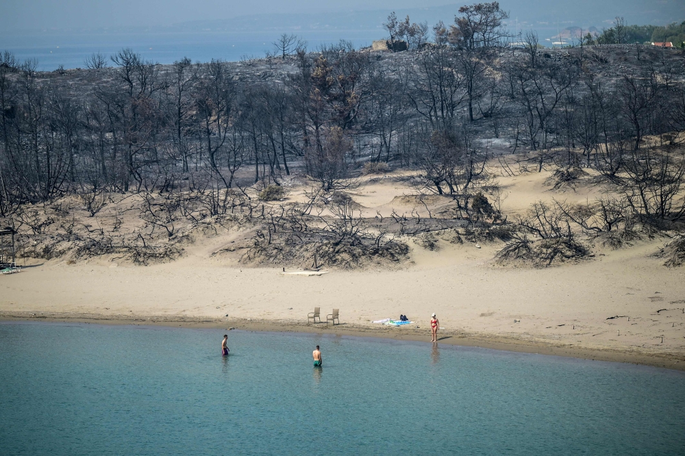 A woman enters the sea from a beach where wildfires destroyed the woods, at Glystra near the village of Gennadi in the southern part of the Greek island of Rhodes, on July 27, 2023. Last month smashed the previous November heat record, pushing 2023’s global average temperature to 1.46 degrees Celsius warmer than pre-industrial levels, the EU’s Copernicus Climate Change Service said. — AFP pic
