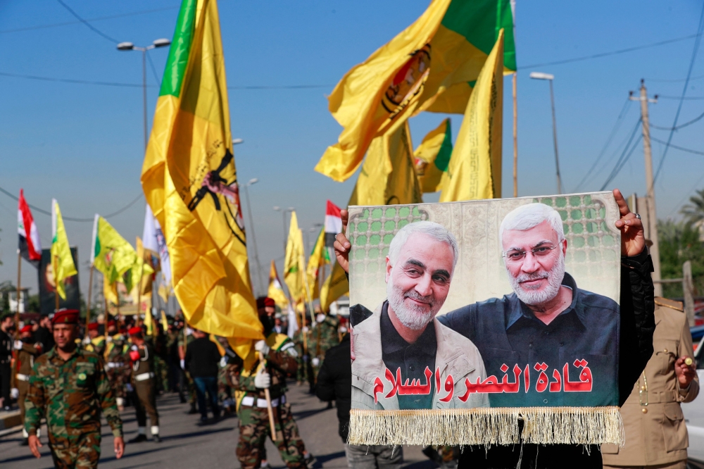 A man lifts a placard depicting slain Iranian commander Qasem Soleimani (left) and Iraqi commander Abu Mahdi al-Muhandis, as fighters bearing flags of Iraq and paramilitary groups, including al-Nujaba and Kataib Hezbollah, march during a funeral in Baghdad for five militants killed a day earlier in a US strike in northern Iraq December 4, 2023. — AFP pic