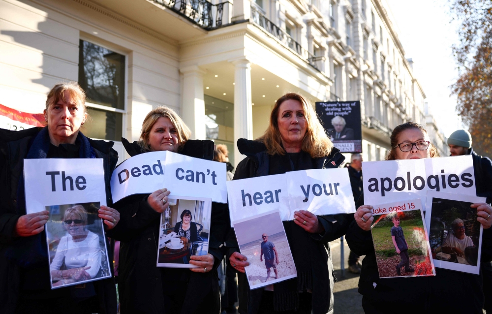 Protesters holds a placard reading ‘The dead can't hear your apologies’ duing a gathering outside the UK Covid-19 Inquiry building in west London, on December 6, 2023 as Britain's former Prime Minister Boris Johnson is inside giving evidence regarding his management of the pandemic. — AFP pic