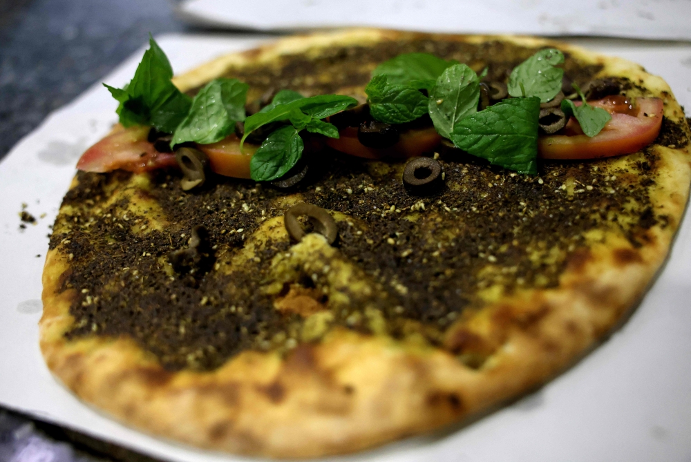 A traditional Lebanese manoushe flatbread topped with mint, tomatoes and olives is displayed on the counter of a bakery in Tabarja north of Beirut on December 6, 2023. — AFP pic