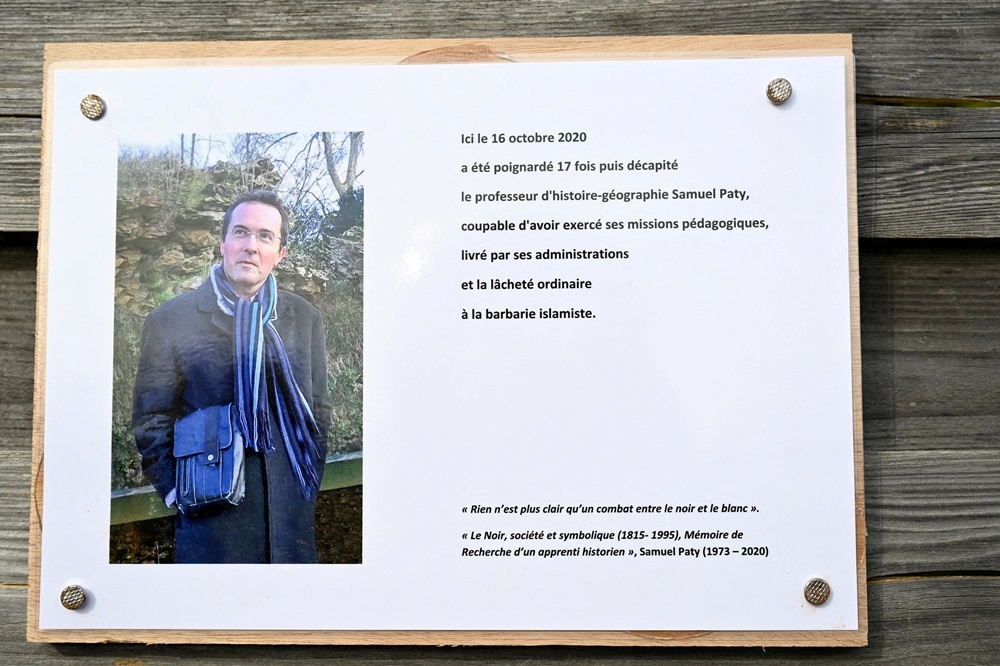 A photograph taken on October 16, 2023 shows a commemorative plaque for slain teacher Samuel Paty (portrait) near the Bois d'Aulne school in Conflans-Sainte-Honorine, outside Paris. ― Bertrand Guay/Pool via Reuters